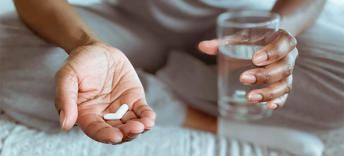 Close-up of woman sitting on bed holding pills and glass of water