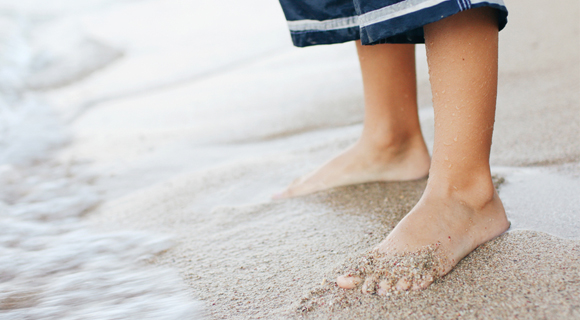 Child's feet in sand at the beach with wave coming on shore