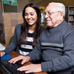 Young woman helping older man use computer.