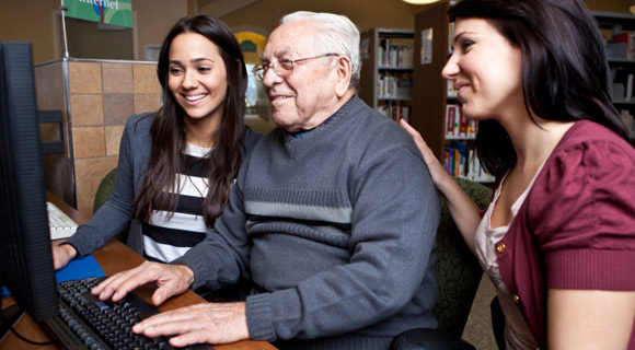 Senior man and two young women inside a library looking at a computer