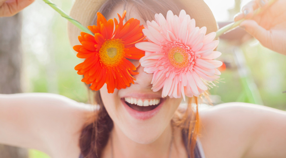 Smiling woman holding sunflowers over her eyes