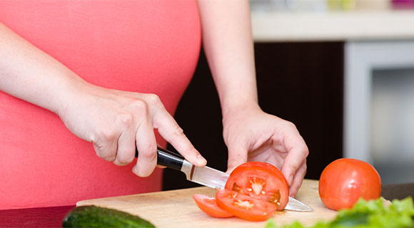 Close-up of pregnant woman slicing vegetables on a cutting board