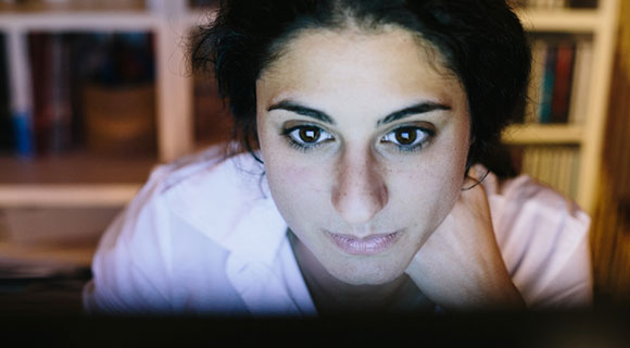 Young woman leaning in close to computer with face lit from screen
