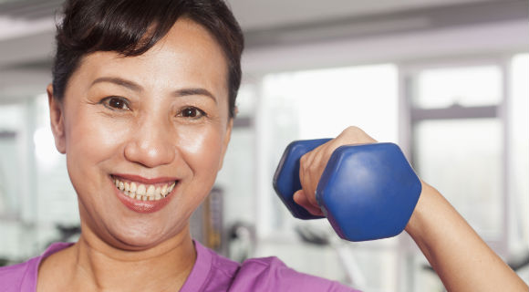 Middle-aged woman smiling while curling bicep with a hand weight
