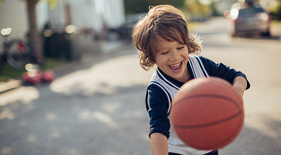 Child playing with a basketball outdoors.