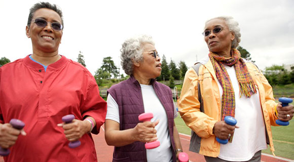 Three women holding hand weights and walking around a track