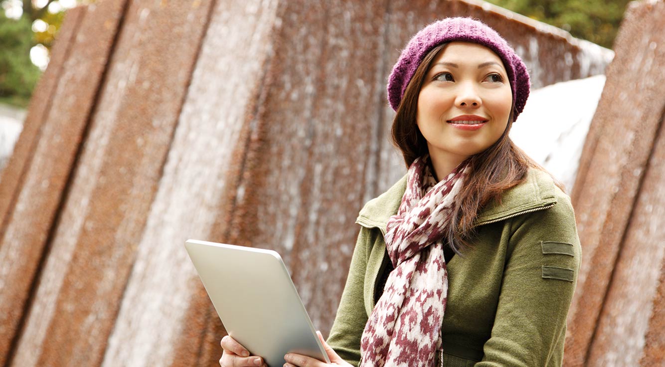 A smiling woman uses her tablet outdoors.