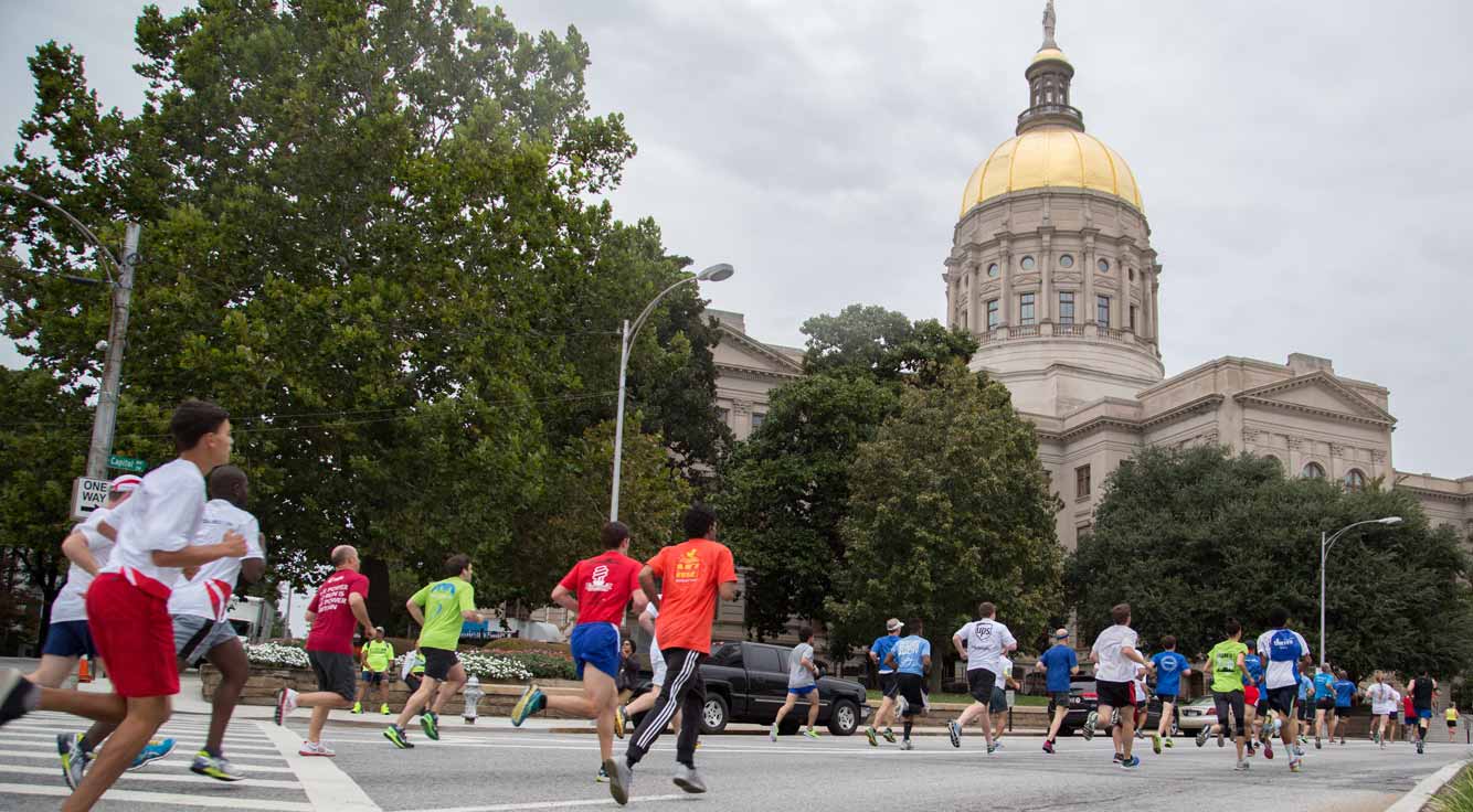 Dozens of race participants run down a tree-lined, city street.
