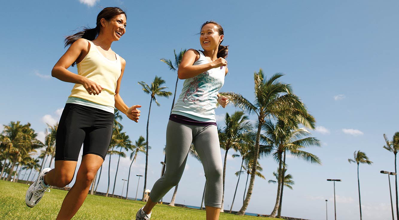 Two beaming women jog past palm trees.