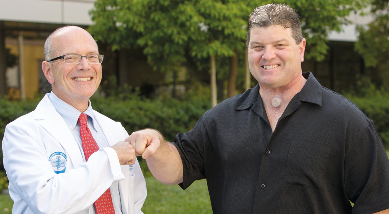 A strapping man fist-bumps his smiling doctor.