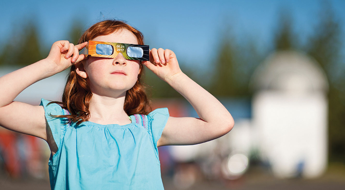 A little girl peers through specialized eclipse glasses.
