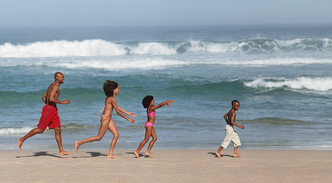 A man, a woman, and two children run along an ocean shore.