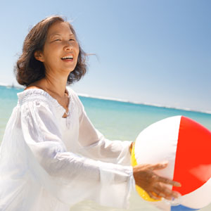 A beaming woman holds a beach ball at the seashore.