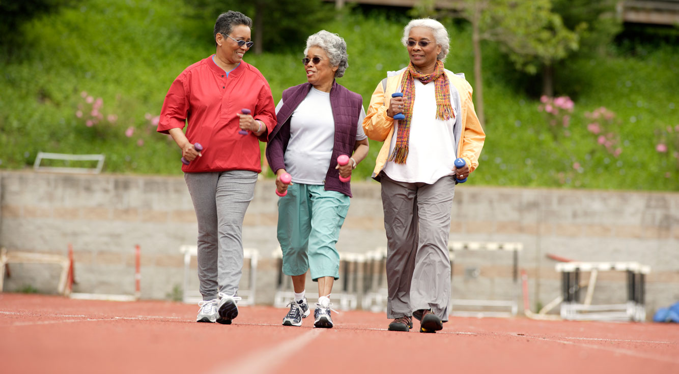 Three women walk outdoors with handweights.