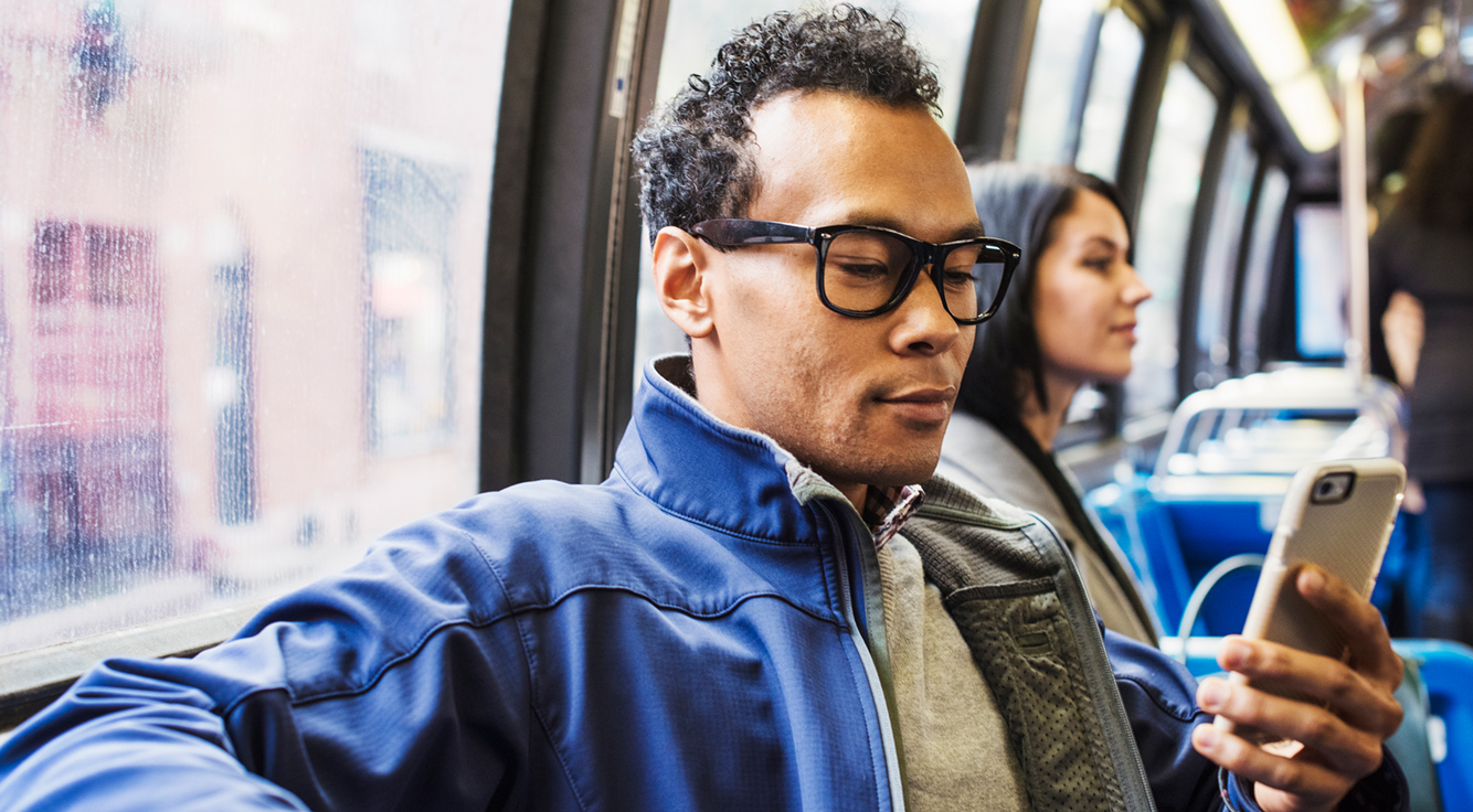 A man riding public transit uses a smartphone.