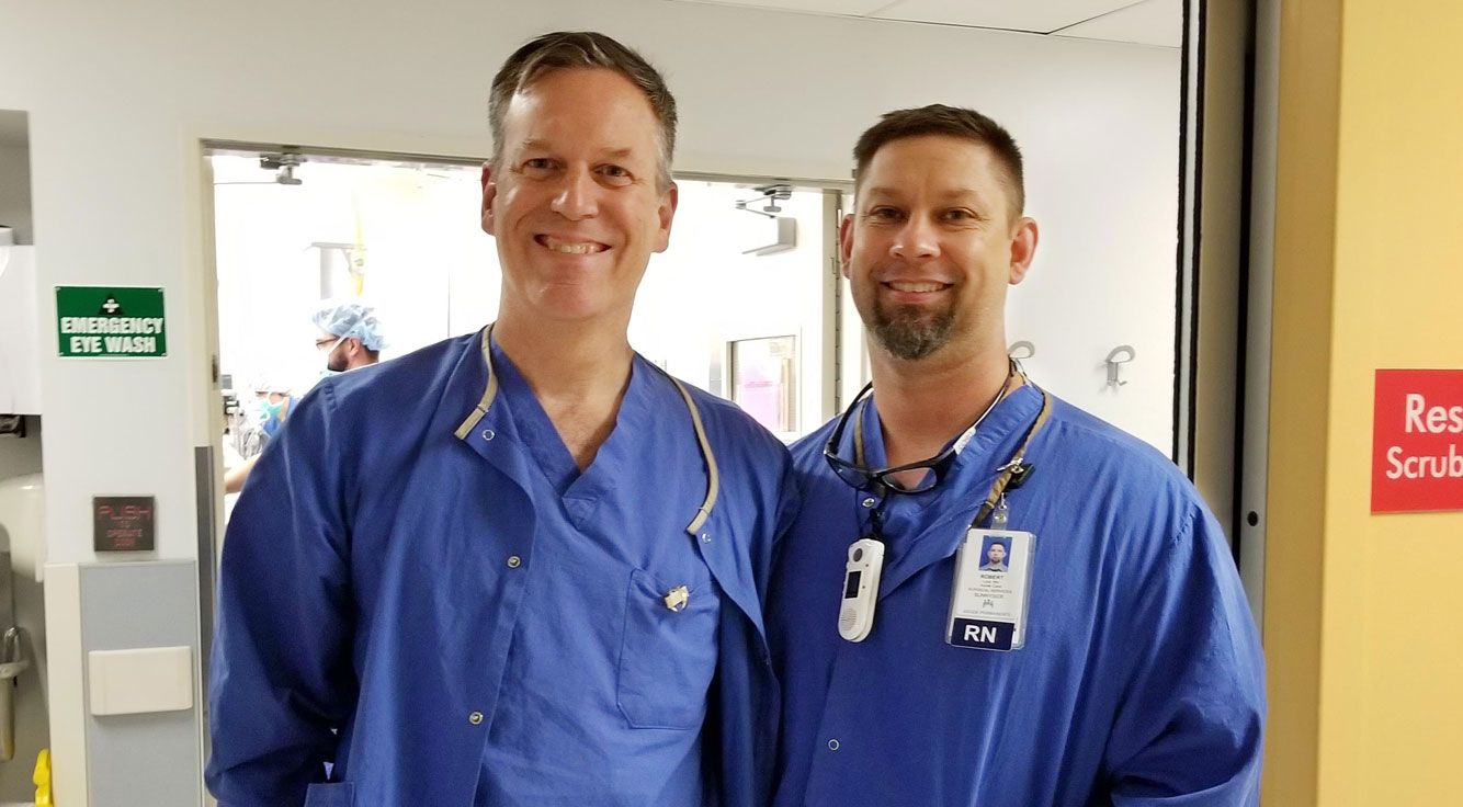 Two men smile in Kaiser Permanente scrubs.