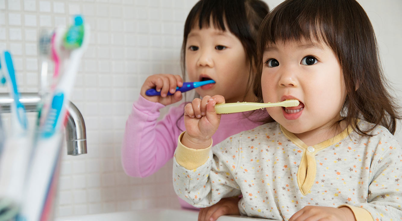 Two small children brush their teeth.