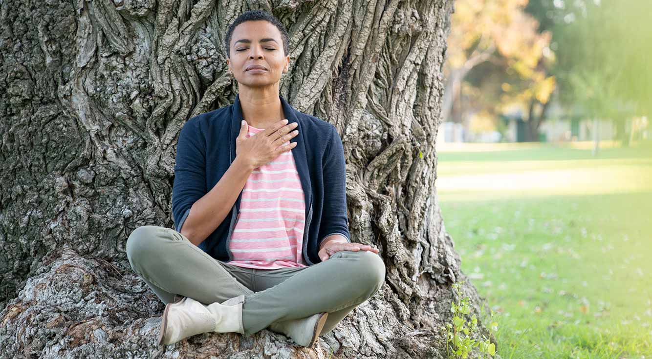 Woman meditating in a park while sitting under a tree.