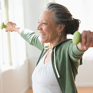 An older woman smiles while lifting two small green weights in her hands.