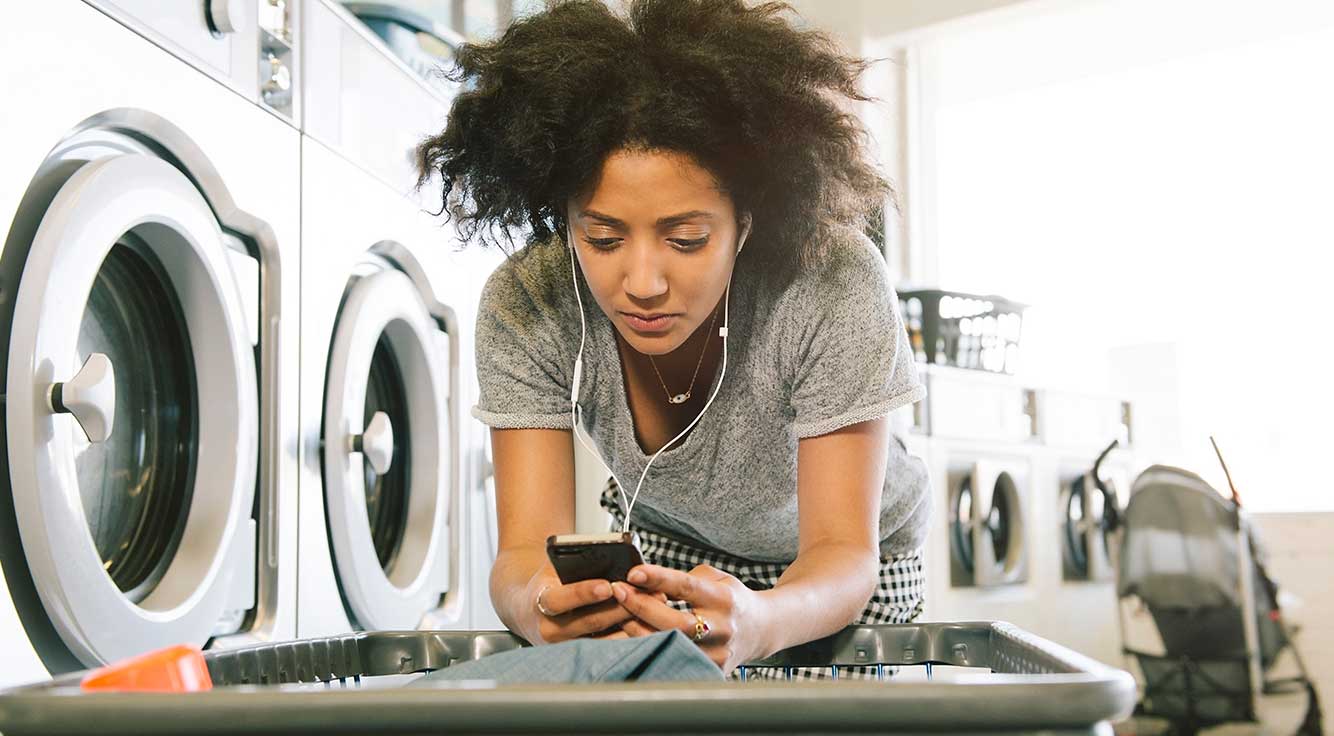 A serious young woman in a laundromat stares at her phone.