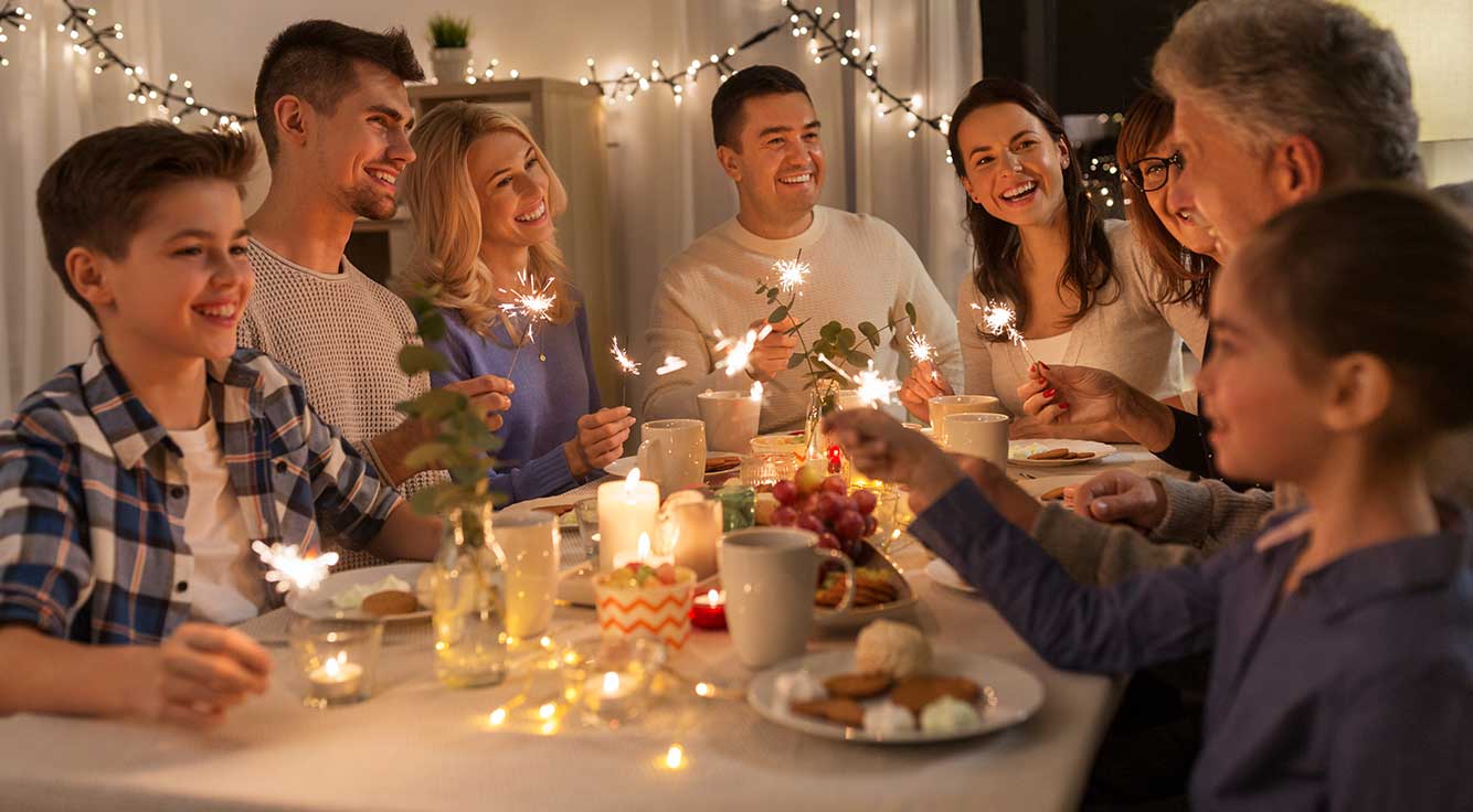 A smiling family sits together at the dinner holding sparklers.