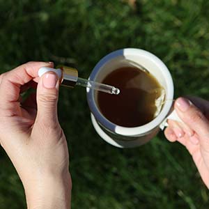 A woman adds a drop of CBD oil to tea