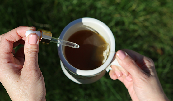 A person adds CBD oil to a cup of tea.