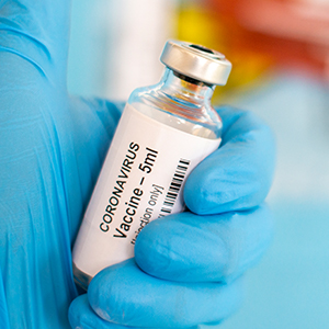 masked hand holding a vial of COVID-19 vaccine