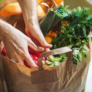 Hands reach into grocery bag full of vegetables