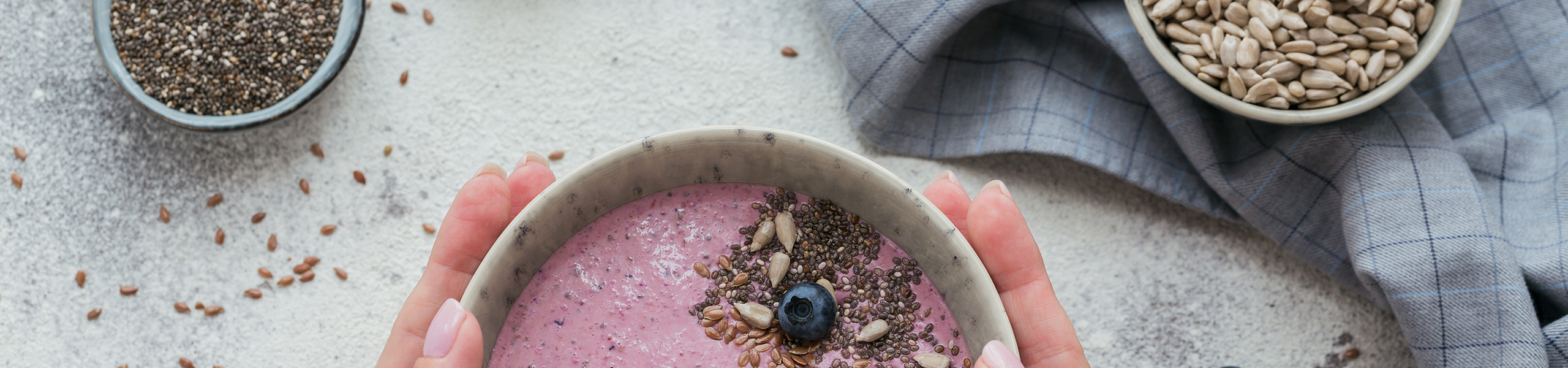 Hands hold a bowl of yogurt topped with flaxseeds and blueberries