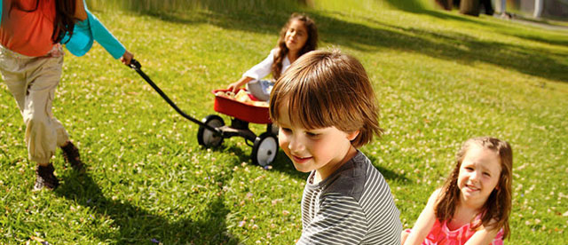 Children racing in red wagons outdoors.