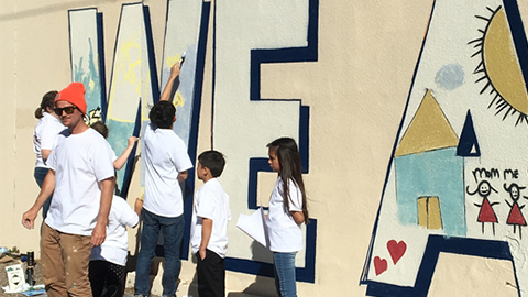 adults and kids painting a mural