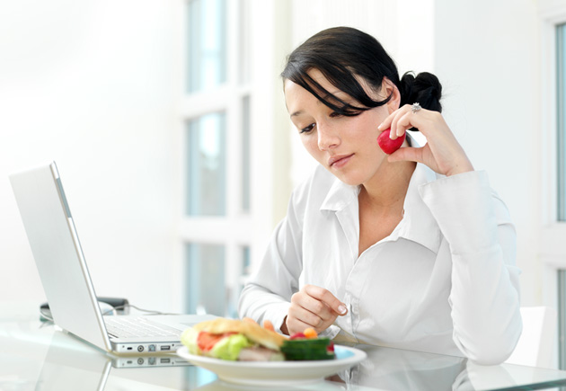 Woman working on laptop at home while eating meal.