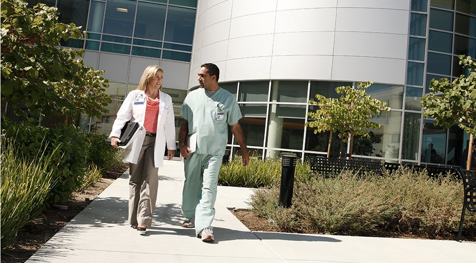 Doctor and specialist communicating while walking outside medical building.
