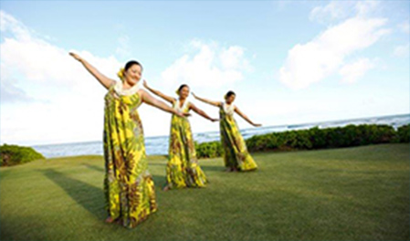 3 women performing hula near ocean.
