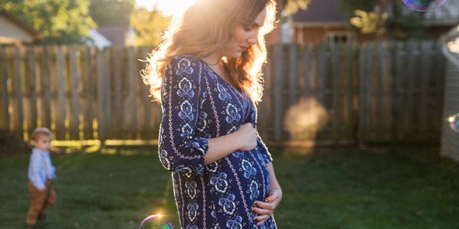A pregnant woman stood on the lawn soaking up the sun.
