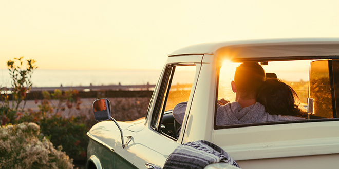 Couple cuddling and enjoying sunset from inside of pickup truck.
