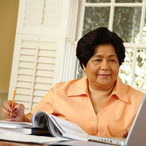 A woman faces a laptop while doing paperwork.
