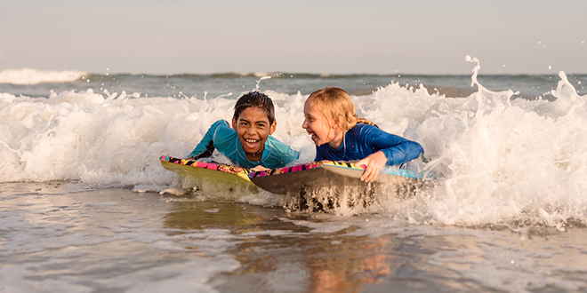 Two children boogie boarding in ocean waves.