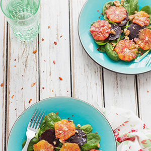 A picnic table with a glass of water and a salad with oranges, walnuts, and spinach.