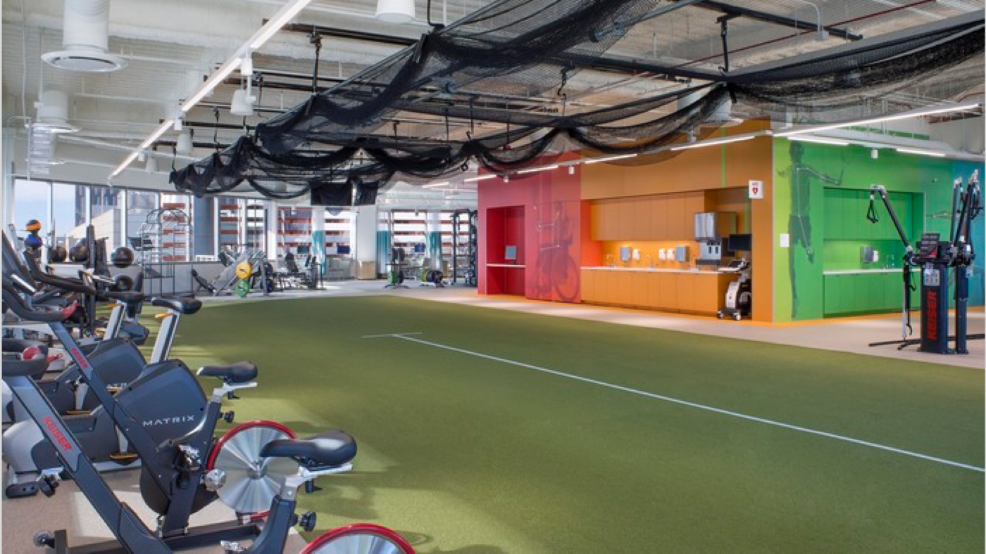 Comprehensive training and rehabilitation gym, with exercise bikes along the edge of a running turf with rainbow painted walls in the background